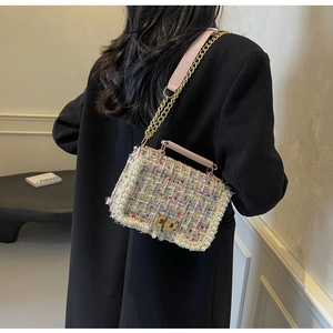 Detail of tweed crossbody bag with pearl trim and gold chain strap worn on black coat