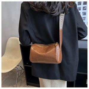 Back view of a woman wearing a brown cylinder crossbody bag with a wide jacquard strap