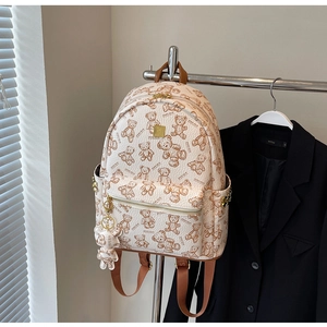 Detail des cremefarbenen Rucksacks mit Teddybär-Print und goldener Logo-Plakette