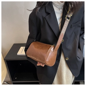 Brown vintage cylinder crossbody bag with ethnic woven strap worn on black blazer