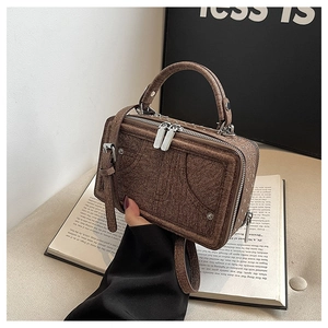 Detail einer braunen strukturierten Box-Handtasche mit silbernen Reißverschlüssen und Gurt