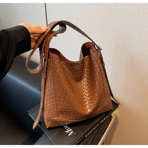 Gros plan d'un sac seau en cuir tressé marron avec une large bandoulière sur canapé