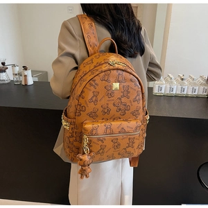 Detail eines braunen Lederrucksacks mit Bärenprints, Goldnieten und einem Bärenanhänger