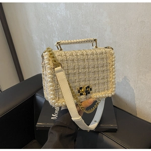 Close-up of cream tweed crossbody bag with pearl trim and gold chain held by model