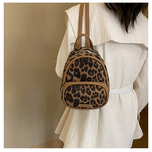 Detail of mini leopard print backpack with brown leather trim worn by model in white dress