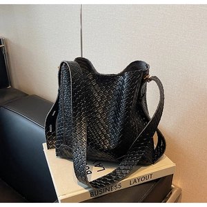 Détail du sac seau tressé noir avec large bandoulière et fermoir en métal doré élégant
