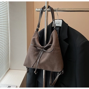 Detailed view of dark brown suede shoulder bag with thin bow detail and adjustable strap