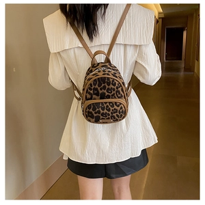 Mini leopard print backpack shown on a model in a cozy indoor setting with brown straps