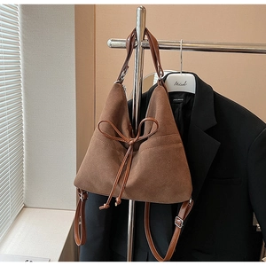 Detail of a brown suede tote bag featuring a decorative bow drawstring and slim leather strap