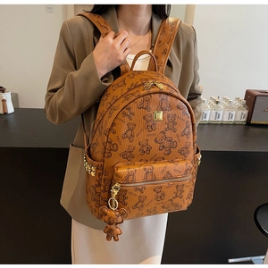 Detail eines braunen Rucksacks mit Teddybär-Print, Goldnieten und Bärenanhänger