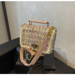 Detail of tweed crossbody bag with pearl trim and golden chain strap held by hand