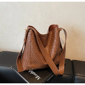 Détail d'un sac hobo en cuir tressé marron sur un banc noir montrant le fini