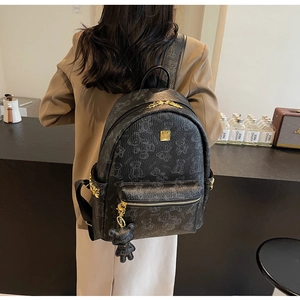Detail eines schwarzen Rucksacks mit Bärenmuster, Goldverzierung und niedlichem Anhänger