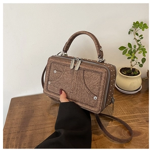 Detailsicht braune Denim-Tasche mit Metallnieten und Tragegriff auf Holzoberfläche
