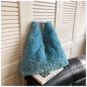 Detailed texture of blue faux fur tote bag placed on a white book and black sofa