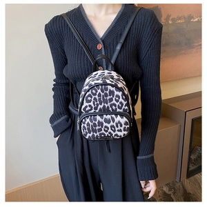 Close-up of mini leopard print backpack featuring metal zippers and logo on model