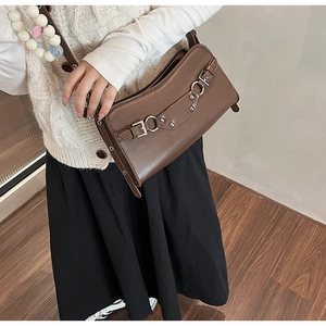 Detail of dark brown leather baguette bag with silver buckles and studs on model