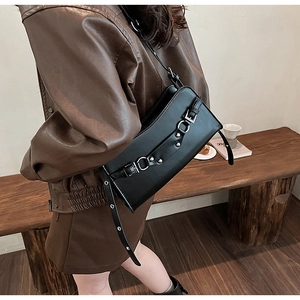 Detail of a black shiny baguette bag with metallic buckle and rivets on a brown leather outfit