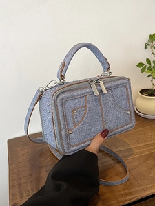 Blaue Denim-Umhängetasche mit silbernen Nieten und braunem Besatz in der Hand