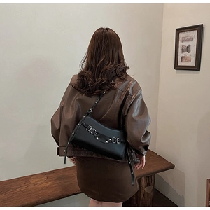 Detail of black leather baguette bag featuring silver buckles and rivets worn by model