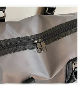 Detail view of smooth dual metal zippers on a gray nylon travel duffel bag with leather trim