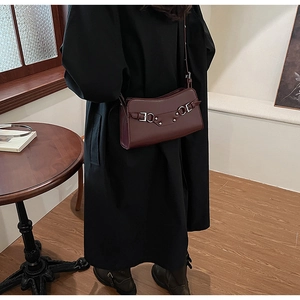 Chic burgundy leather baguette bag with metal buckle detail worn over a black coat