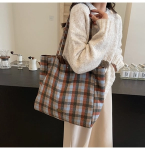 Detail of checkered tote bag showing thick wool fabric and oval metal plaque decoration