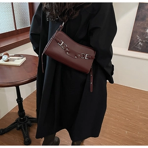 Detail of burgundy leather baguette bag with silver hardware on a model in a cozy room