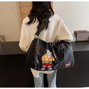 Detail of a black travel bag featuring an embroidered bear and metal stud accents