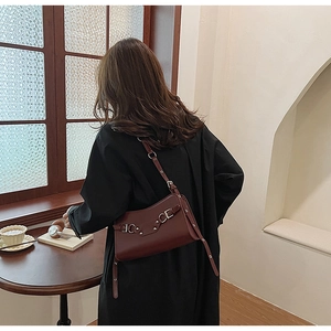 Detail of dark burgundy leather baguette bag with silver rivets worn by a model in a cafe