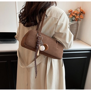 Close-up of brown suede shoulder bag with creative baseball theme pendants on a model