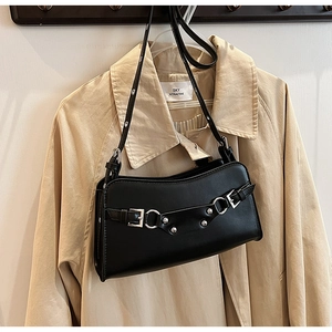 Detail of black faux leather baguette bag with silver buckles hung on a beige trench coat