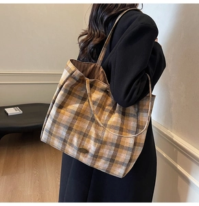 Detail of a large yellow plaid tote bag with metal emblem shown on female model's shoulder