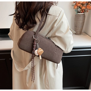 Details der dunkelbraunen Canvas-Schultertasche mit dekorativen Anhängern am Trenchcoat