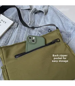 Détail de la poche zippée arrière d'un sac bandoulière en nylon vert contenant un téléphone