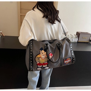 Close-up of grey travel bag with bear embroidery and metal rivet details on strap