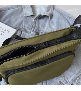 Détail du sac à bandoulière en toile vert foncé montrant la double fermeture éclair