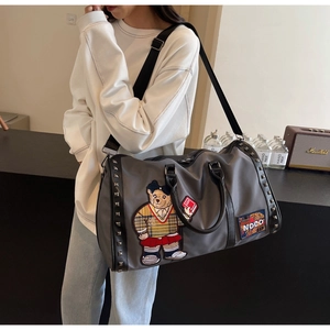 Detail of dark grey travel bag with bear embroidery and decorative metal rivets