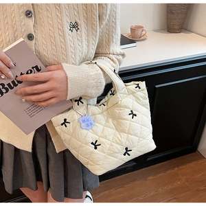 Detail of cream quilted tote bag with black bow embroidery and blue floral charm