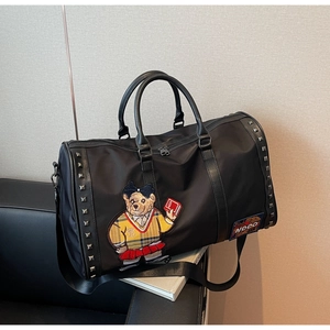 Close-up of black duffel bag featuring a teddy bear embroidery and metal rivet details