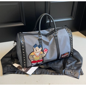 Detail of gray nylon travel bag featuring embroidered bear patch and square metal rivets