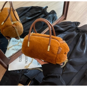 Detail of a brown faux fur cylinder handbag with golden zipper and metal chain strap