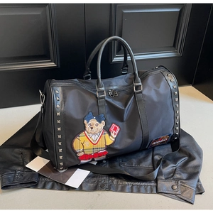 Macro detail of black travel bag featuring bear embroidery and metal rivet accents
