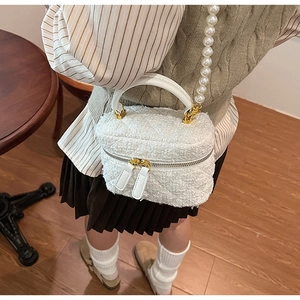 Gros plan du sac seau en peluche blanche avec bandoulière en perles et poignée en cuir