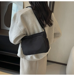 Détail de la sacoche noire en nylon avec poche zippée à l'avant et bandoulière réglable