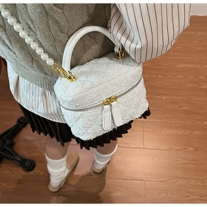 Gros plan du sac seau en tweed blanc avec bandoulière en perles et double zip doré brillant