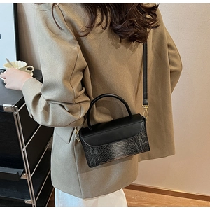Detail view of black vintage bag with faux crocodile skin texture and gold hardware on model