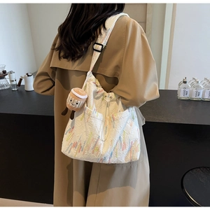 Detail of white textured fabric tote with colorful embroidery and plush coffee cup charm