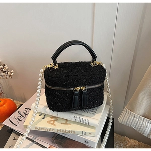Détail du sac seau en tweed noir avec bandoulière en perles sur livre ancien