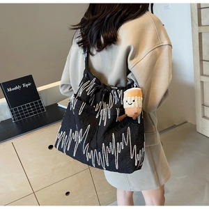 Detail of black tote bag with wave embroidery and plush coffee cup charm on strap